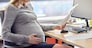 pregnancy, business and work concept - smiling pregnant businesswoman sitting at office table and reading papers