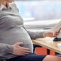 pregnancy, business and work concept - smiling pregnant businesswoman sitting at office table and reading papers