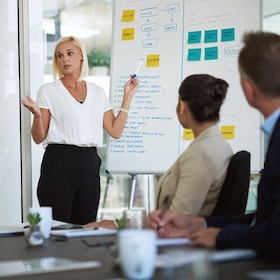 Presentation, woman and whiteboard with staff in office for workflow steps, diagram and teamwork for web design. Female speaker, people and meeting of strategy process, chart and interface project.