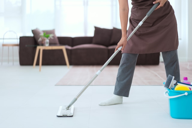 Maid using mop with bucket plastic of cleaner equipment to mopping cleanup floor in living room.