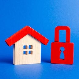 A wooden house and a red padlock. Unavailable and expensive real estate. house Insurance. Security and safety. Confiscation for debts. alarm system. seizure of property. Protection of property rights.