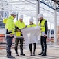 Front view of group of engineers with blueprints standing on construction site.