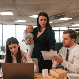 Beautiful mother is holding her son. Infant baby is in the office where group of people are working together.