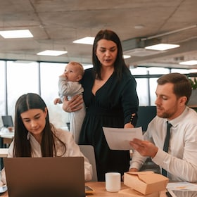 Beautiful mother is holding her son. Infant baby is in the office where group of people are working together.