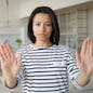 Serious young woman showing stop hand warning gesture, protesting against domestic violence or abortion. Strict female says no to abuse and discrimination, expressing disagreement, standing at home.