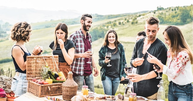 Happy adult friends eating at picnic lunch in italian vineyard outdoor - Young people having fun on gastronomic weekend tuscany tour - Friendship, summer and food concept - Focus on center guys