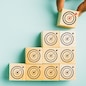 Close-up of a man's hand arranging wooden blocks in a stair-like formation, placing a cube with a target icon on top. Depicting growth, success, and strategic concepts. Isolated on a blue background.