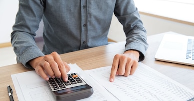 Close-up of unrecognizable man working with financial data. He using calculator and examining document. Financial inspector holding examination. Paperwork or finance concept