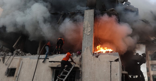 Il personale della protezione civile perlustra una casa in fiamme colpita dai raid aerei israeliani nella città di Gaza. L’agenzia di protezione civile di Gaza ha dichiarato che 21 persone sono state uccise e decine ferite in diversi raid aerei israeliani sul territorio palestinese il 22 novembre. (Foto di Omar AL-QATTAA / AFP)