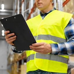 logistic business, shipment and people concept - close up of male worker or supervisor with clipboard in reflective safety vest at warehouse