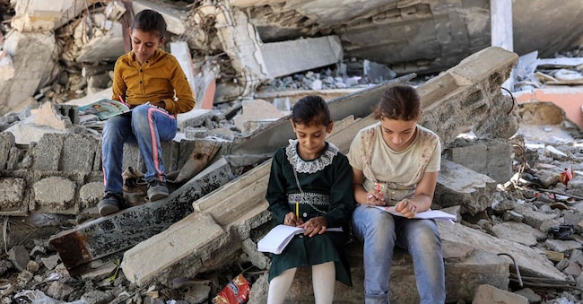 Bambini scrivono su quaderni tra le macerie di edifici distrutti vicino a una tenda utilizzata come centro educativo di fortuna per gli studenti delle elementari a Jabalia, nel nord della Striscia di Gaza, l'8 settembre 2024, nel corso della guerra in corso nel territorio palestinese tra Israele e Hamas. Gli attacchi militari israeliani hanno ucciso molti palestinesi che si rifugiavano nelle scuole e Israele sostiene che i combattenti di Hamas si nascondono in queste strutture (Foto di Omar AL-QATTAA / AFP)