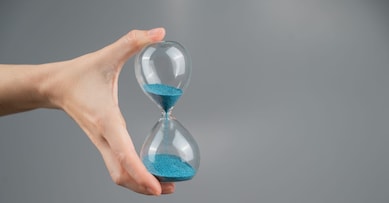 Woman holding an hourglass on a gray background. Close-up. Copy space