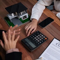 Reviewing house loan contract with agent. Analyzing financial documents and tax rates with calculator for ownership of property. Key signature for new home purchase and financing. Enthusiastic