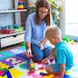 Young caucasian child playing at playschool with teacher. Mother and son playing with wooden pieces train at playroom