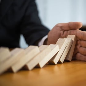 Businessman hand stops domino continuous overturned meaning that hindered business failure. Stop over this business failure concept.
