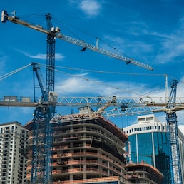 Cranes on modern skyscraper construction in city at sunny day with blue sky