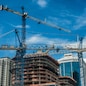 Cranes on modern skyscraper construction in city at sunny day with blue sky