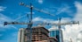 Cranes on modern skyscraper construction in city at sunny day with blue sky