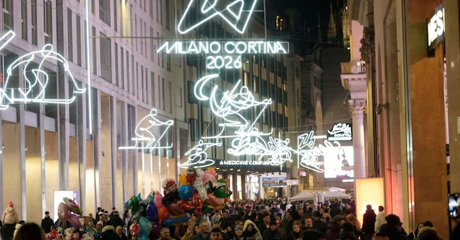 La gente passeggia lungo Corso Vittorio Emanuele II, la principale via del centro di Milano, mentre le insegne al neon con il simbolo olimpico sono appese in vista delle prossime Olimpiadi invernali di Milano-Cortina, (AP Photo/Luca Bruno)   