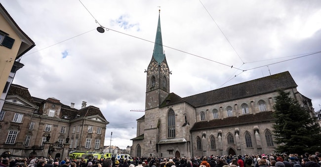 La gente osserva la torre Fraumuenster durante i 5 minuti di rintocchi di campane in occasione della cerimonia commemorativa e della giornata nazionale di lutto seguita al tragico incendio del bar “Le Constellation” a Crans-Montana, nella Muensterplatz a Zurigo, Svizzera, il 9 gennaio 2026. 40 persone, per lo più adolescenti, hanno perso la vita e 116 sono rimaste gravemente ferite nell’incendio del bar “Le Constellation” durante i festeggiamenti di Capodanno nella località turistica svizzera di Crans-Montana, nelle Alpi. 