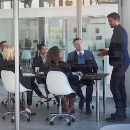 Executive, meeting and group in office room for corporate planning, strategy or business training. Management, people at table and businessman or speaker, mentor and professional advice to company.