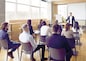 Team of people having class with business trainer. Group of male and female employees sitting at desks in modern office and listening to lecture by experienced teacher sharing knowledge and guidance