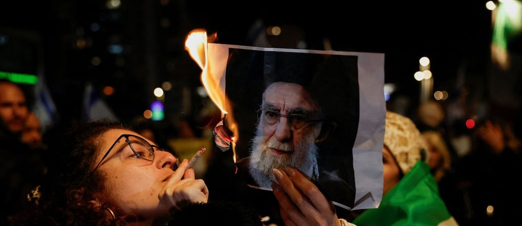 Una donna accende una sigaretta con il fuoco di una foto in fiamme del leader supremo iraniano Ayatollah Ali Khamenei, mentre gli israeliani si radunano a sostegno delle proteste nazionali in corso in Iran, a Holon, Israele, il 14 gennaio 2026. REUTERS/Ammar Awad