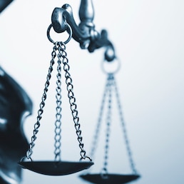 Close up detail of the scales of justice being held aloft by a small statue of Justice over a grey background with copy space conceptual of law and order