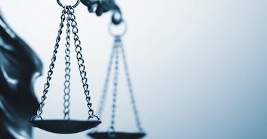 Close up detail of the scales of justice being held aloft by a small statue of Justice over a grey background with copy space conceptual of law and order