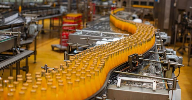 Interno di una fabbrica di bevande. Nastro trasportatore con bottiglie di succo.