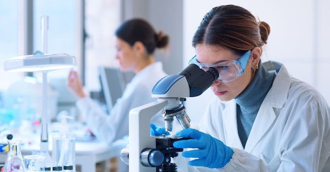 Young scientists conducting research investigations in a medical laboratory, a researcher in the foreground is using a microscope