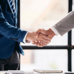 Two men shake hands in a business meeting. Scene is professional and formal. The handshake symbolizes agreement and trust between the two men