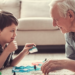 Grandpa and grandson are playing with toys, looking at each other and smiling while resting together at home