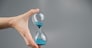 Woman holding an hourglass on a gray background. Close-up. Copy space