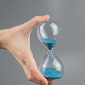 Woman holding an hourglass on a gray background. Close-up. Copy space