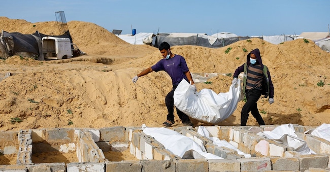 Persone trasportano un cadavere durante una sepoltura di massa di palestinesi non identificati, i cui corpi sono stati rilasciati dopo essere stati trattenuti in Israele durante la guerra, a Deir Al-Balah, nella Striscia di Gaza centrale, il 13 febbraio 2026. REUTERS/Mahmoud Issa