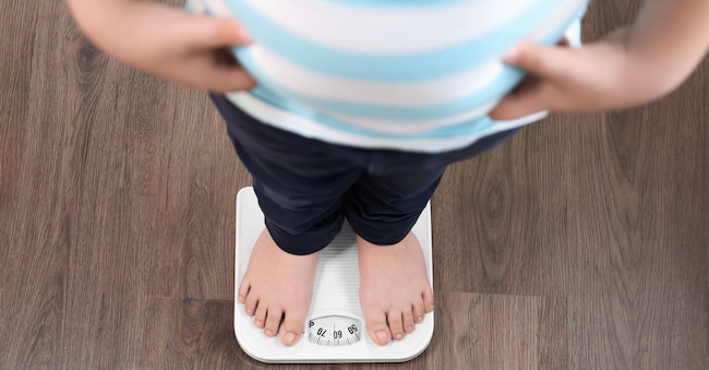 Ragazzo in sovrappeso in piedi su una bilancia (Adobe Stock)