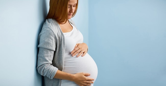 Blond pregnant woman leaning on to blue wall caressing her big belly gently pressmaster - stock.adobe.com