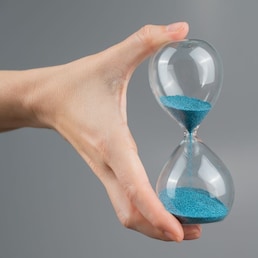 Woman holding an hourglass on a gray background. Close-up. Copy space Михаил Решетников - stock.adobe.com