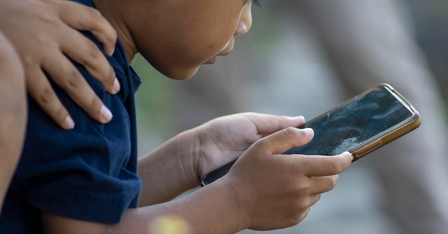 Un bambino utilizza uno smartphone nel parco di Denpasar, a Bali (foto Epa) EPA
