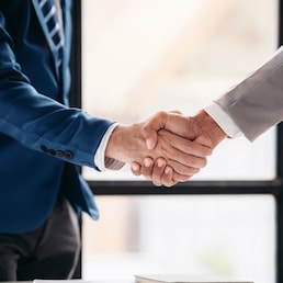 Two men shake hands in a business meeting. Scene is professional and formal. The handshake symbolizes agreement and trust between the two men Freedomz - stock.adobe.com