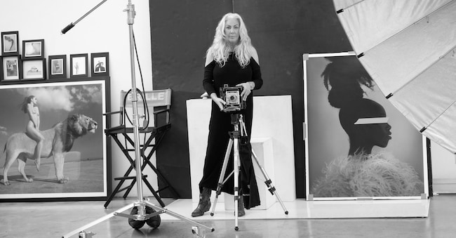 Sylvie Blum nel suo studio di Hollywood con la sua macchina fotografica analogica vintage Crown Graphic per le Polaroid di grande formato. Dietro di lei, a sinistra “Angela Rides the Lion” (2008), che fa parte della collezione del MOCA di Bangkok. A destra, “Hair Sculpture” della sua nuova serie “Pink Tape”: gli occhi della musa, coperti di nastro adesivo rosa, sono un omaggio alla Pop Art e aggiungono un tocco di mistero. 