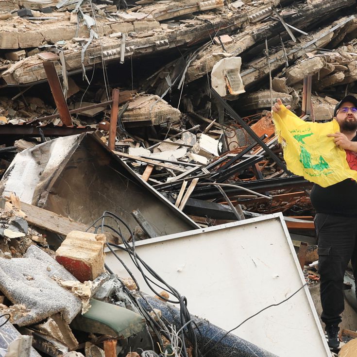 A man holds a Hezbollah flag while standing on the rubble of a damaged building, after a 10-day ceasefire between Lebanon and Israel went into effect, in the southern suburbs of Beirut, Lebanon, April 17, 2026. REUTERS/Adnan Abidi REUTERS