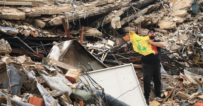 A man holds a Hezbollah flag while standing on the rubble of a damaged building, after a 10-day ceasefire between Lebanon and Israel went into effect, in the southern suburbs of Beirut, Lebanon, April 17, 2026. REUTERS/Adnan Abidi REUTERS