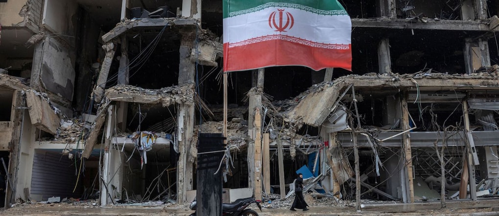 Una bandiera iraniana sventola mentre una donna passa davanti a edifici danneggiati durante una tregua di dieci giorni tra Libano e Israele, nella periferia sud di Beirut, in Libano, il 20 aprile 2026. REUTERS/Marko Djurica REUTERS