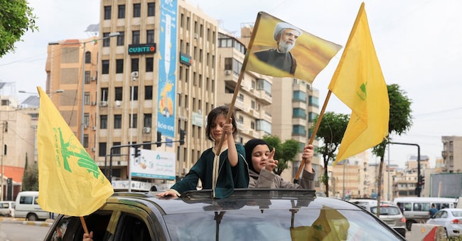 Bambini con in mano bandiere di Hezbollah stanno in piedi su un veicolo mentre gli sfollati si dirigono verso le loro case dopo l'entrata in vigore di una tregua di 10 giorni tra Libano e Israele, nella periferia meridionale di Beirut, Libano, 17 aprile 2026.  (Reuters)