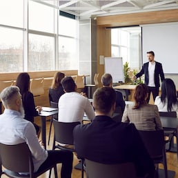 Team of people having class with business trainer. Group of male and female employees sitting at desks in modern office and listening to lecture by experienced teacher sharing knowledge and guidance Studio Romantic - stock.adobe.com