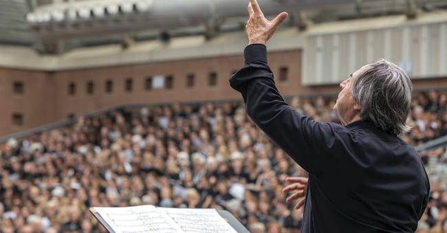 Viaggio nella coralità. Con il progetto «Cantare amantis est» il Maestro Riccardo Muti (di profilo) dirige oltre 3500 coristi al Pala De André di Ravenna (Silvia Lelli)