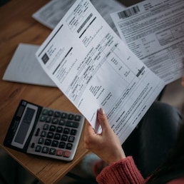 Close-up of female hands with pay slips, utility bills, account statements, payment receipts. A woman makes a count of household, family expenses with a calculator at home on the table. Anna - stock.adobe.com