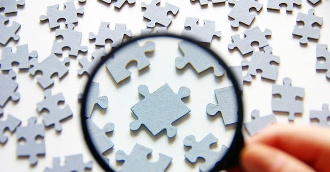 Hand with magnifying glass and puzzle isolated on white background